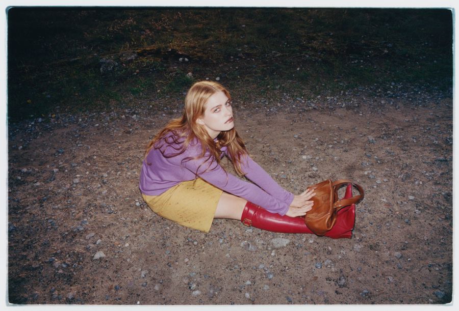 Editorial portrait of a model with long wavy hair sitting on gravel