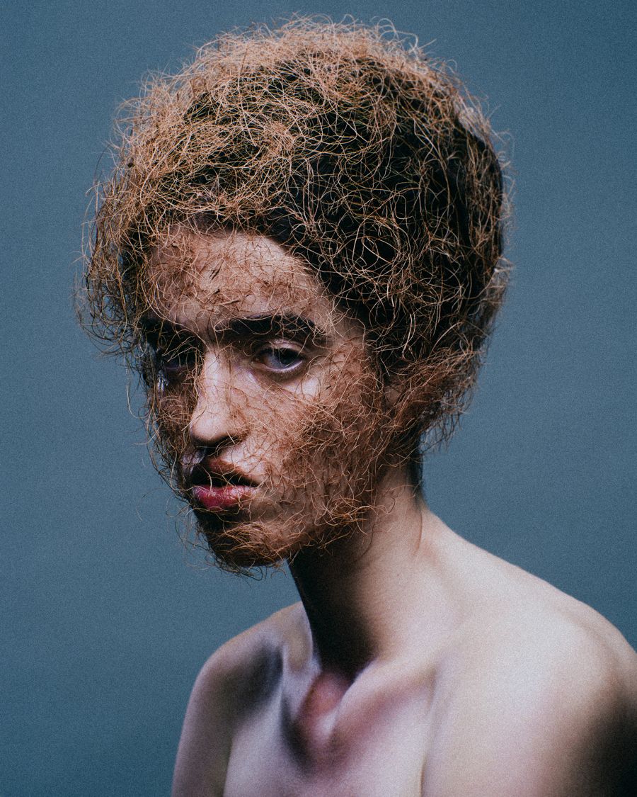 Avant-garde hair and face covered in fine fibres against a blue backdrop